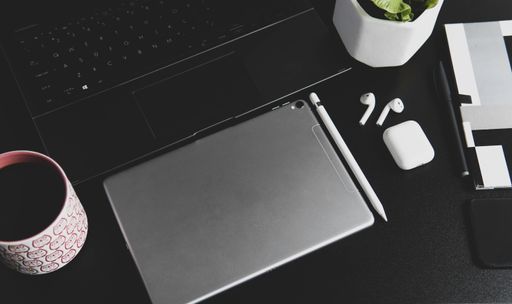 A top view of a tablet with wireless earphones and a pen near the laptop on the table
