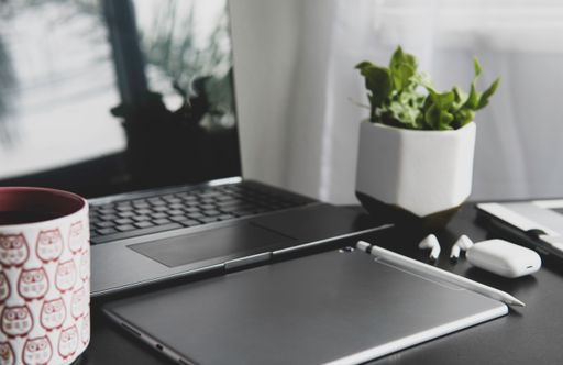 A closeup shot of a tablet with wireless earphones and a pen near the laptop on the table