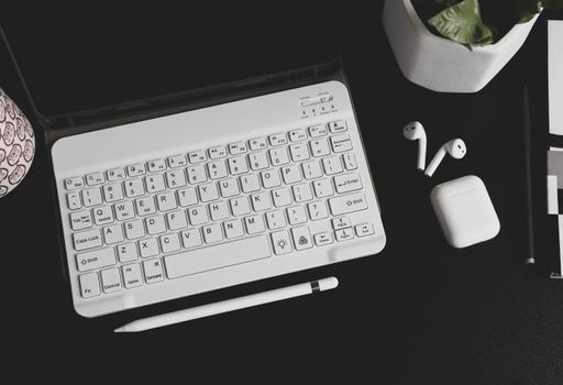 A top view of a laptop with wireless earphones and a pen on the table