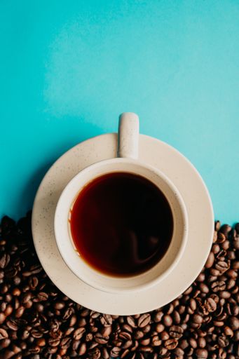 A closeup overhead shot of a cup of coffee with coffee beans on a blue background