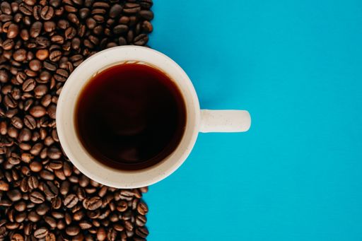 A closeup overhead shot of a cup of coffee with coffee beans on a blue background