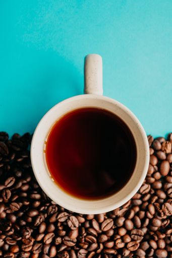 A closeup overhead shot of a cup of coffee with coffee beans on a blue background
