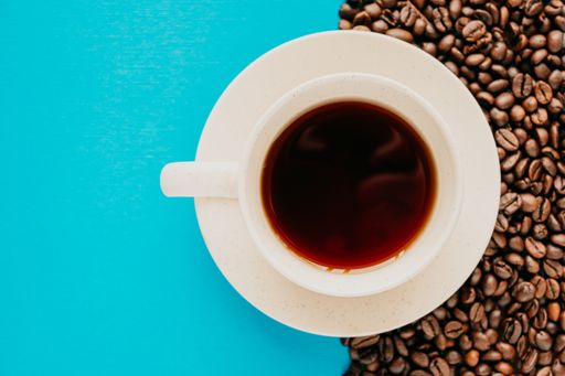 A closeup overhead shot of a cup of coffee with coffee beans on a blue background