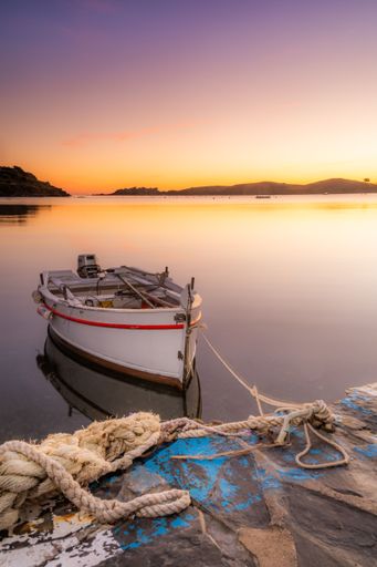 A serene sunset view of a small boat tied to a dock with calm waters and hills in the background.