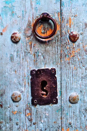 Close-up of an antique wooden door with a rustic metal knocker and keyhole, showcasing weathered textures and vibrant colors.