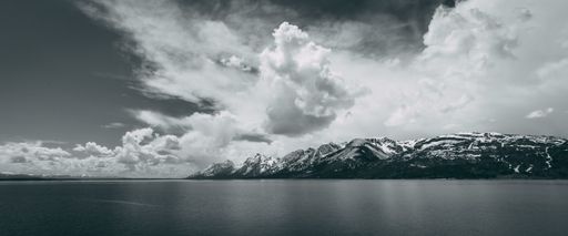 A grayscale shot of a snowy mountain from the ocean on a cloudy day
