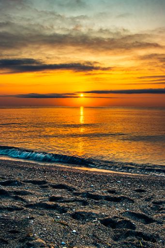 A beautiful view of a sandy beach with a calm sea view and cloudy sky in the background at sunset