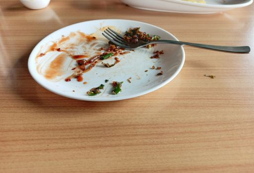 Selective Focus of white plate with small pieces of left over food with a fork and other cutleries in the background blurred