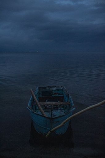 An eerie shot of a docked small blue boat in the sea on a gloomy day