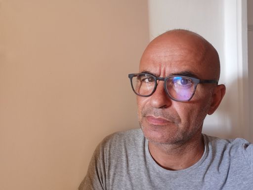 A portrait of a Hispanic bald male with sunglasses and a cautious facial expression