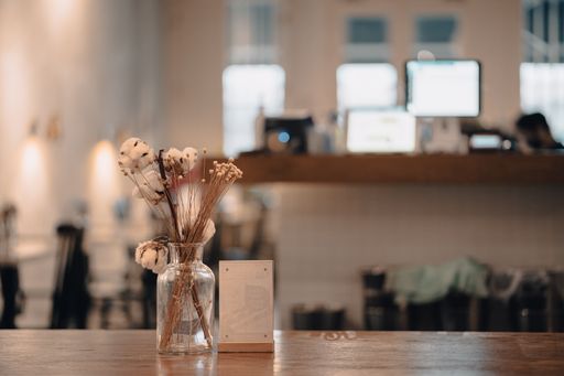 A closeup shot of a cafe wooden table with a jar of decorative flowers against a blurred background