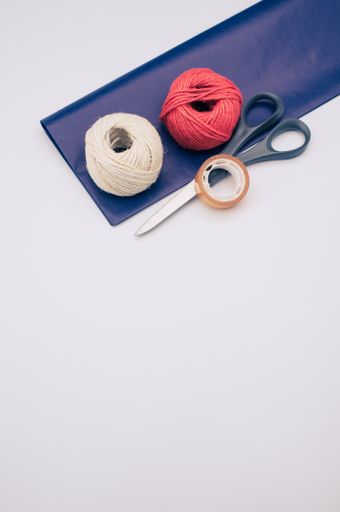 decorative yarn balls with blue paper sheet scissors and tape on a white surface