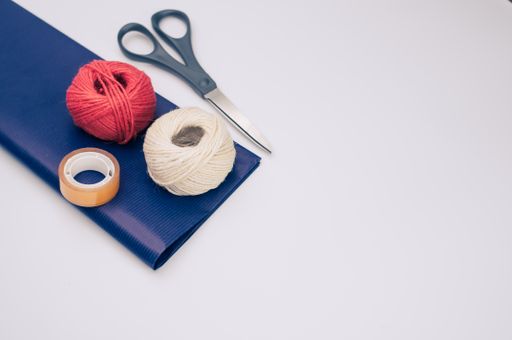 decorative yarn balls with blue paper sheet scissors and tape on a white surface