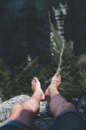 A vertical shot of a guy wearing shorts sitting on a rocky peak on a sunny day