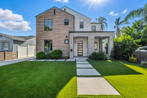 Modern suburban home with a manicured lawn and clear sky, featuring contemporary architecture and lush greenery.