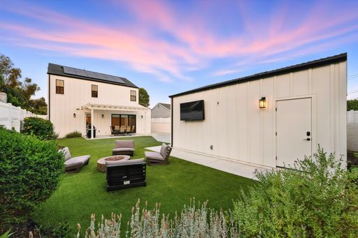 A manicured backyard with a white detached garage, a small paved area, and a patio set under a sunset sky.