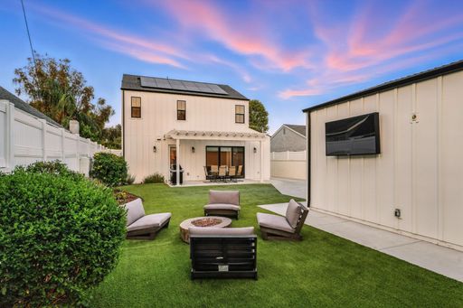 A manicured backyard with a white detached garage, a small paved area, and a patio set under a sunset sky.