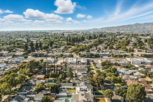 An aerial view of a suburban neighborhood with many trees and houses, set against a backdrop of mountains.