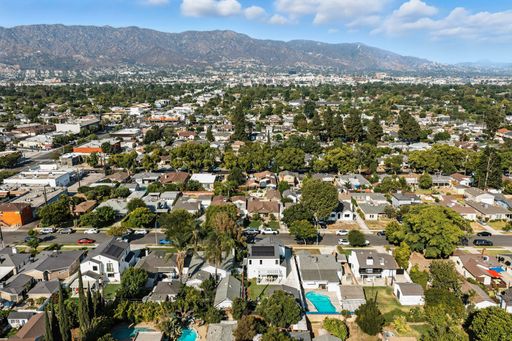 An aerial view of a suburban neighborhood with many trees and houses, set against a backdrop of mountains.
