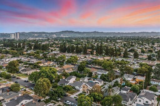 An aerial view of a suburban neighborhood with tree-lined streets and houses, under a dramatic, colorful sky at sunset.