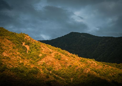 A scenic view of lush green mountains under a dramatic sky with sunlight highlighting the landscape.