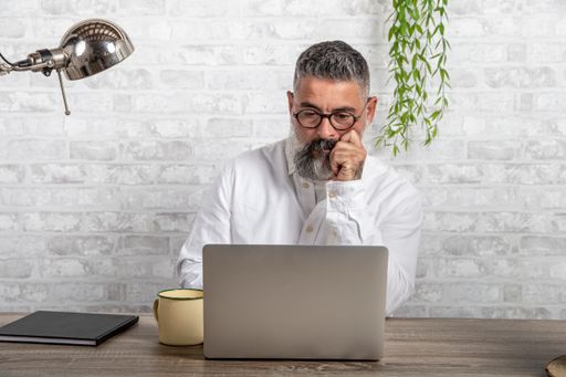 A bearded man working from home in front of his desk with a laptop