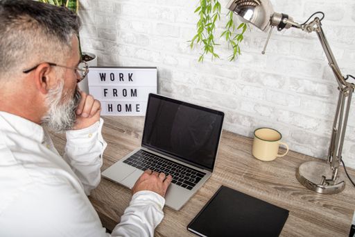 A bearded man working from home in front of his desk with a laptop