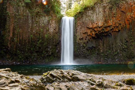A stunning waterfall cascading into a serene pool surrounded by rocky cliffs and lush greenery.