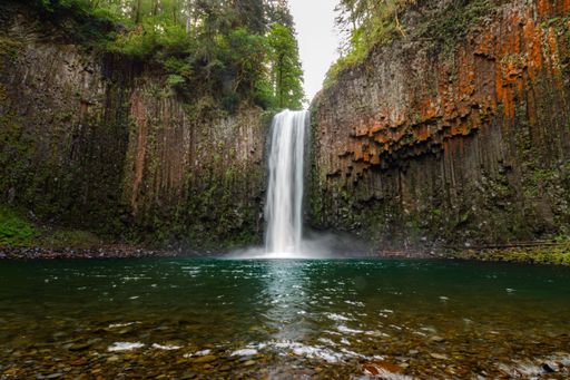 A stunning waterfall cascades into a clear pool surrounded by lush greenery and rocky cliffs, creating a serene natural landscape.