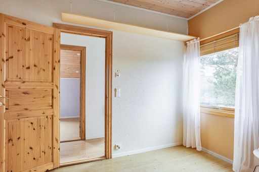 A daylight shot of an empty room with an open door and an outside view from the window