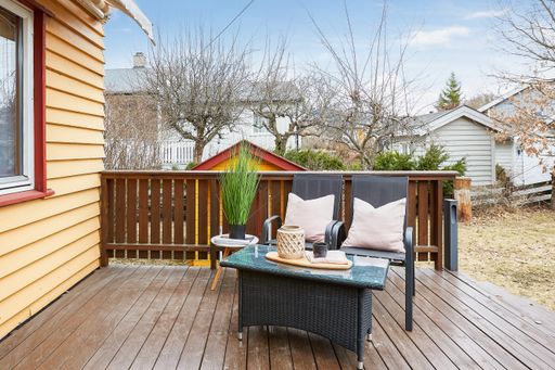 A daylight shot of a table and two chairs with pillows in the balcony of a house