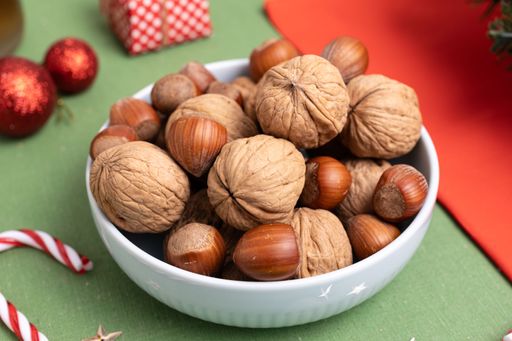 A close-up of a bowl filled with hazelnuts and walnuts on a festively adorned Christmas table