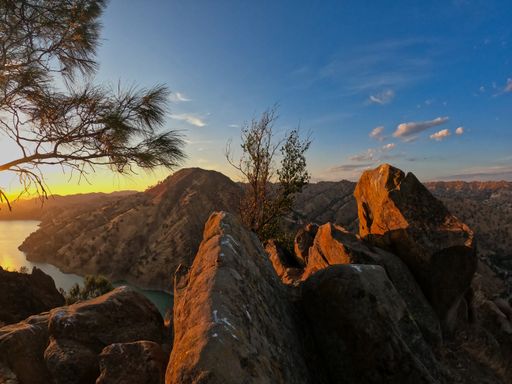 A beautiful shot of rocks with trees under a blue cloudy sky during the sunset