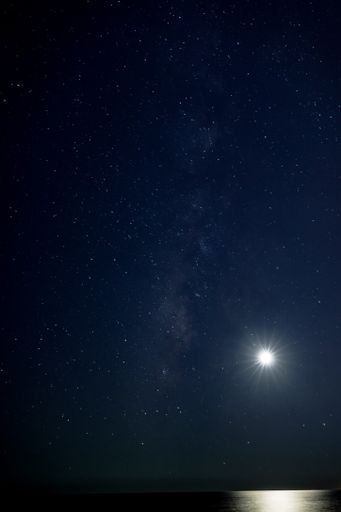 A vertical shot of the moon shining above the calm sea