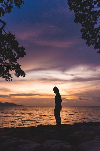 A vertical shot of the woman's silhouette against the beautiful sunset above the sea.