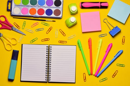 A top view of a blank notebook and various school supplies on a yellow surface - copy space