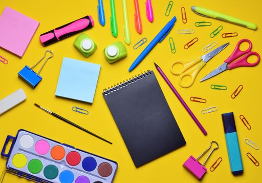 A top view of a black notebook and various school supplies on a yellow surface - copy space