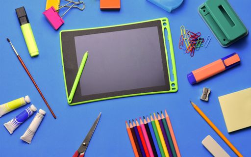 A top view of a tablet and various school supplies on a blue surface - copy space