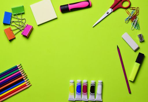A top view of various types of school supplies on a green surface with copy space