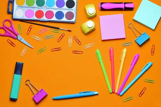 A top view of various types of school supplies on an orange surface with copy space