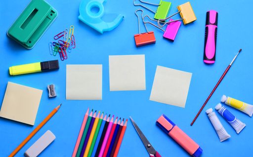 A top view of blank sticky notes and various school supplies on a blusurface - copy space