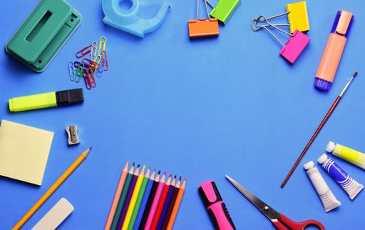 A top view of various school supplies on a blue surface - copy space