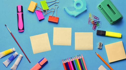 A top view of blank sticky notes and various school supplies on a blue surface - copy space