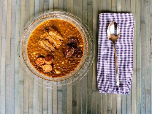 A closeup shot of delicious lentil soup on a plate with cabbage and a silver spoon on the side