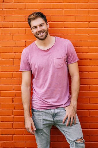 A young Caucasian stylish man wearing a nice pink t-shirt posing against an orange wall