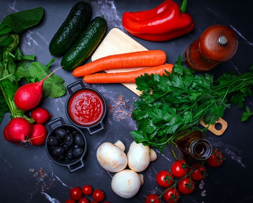 A vibrant assortment of fresh vegetables and herbs with spices on a dark marble surface.