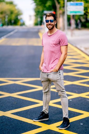 A young Caucasian stylish man wearing a nice pink t-shirt and sunglasses walking on a street