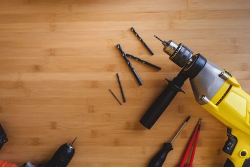 Flat lay view of drills with different drills and screwdrivers lying on a wooden table top.