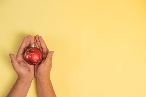 A closeup of the hands holding a red bauble isolated on yellow background.