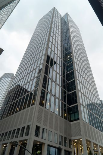 A vertical low angle shot of skyscraper under a gloomy sky in Frankfurt, Germany with lights reflected in its windows